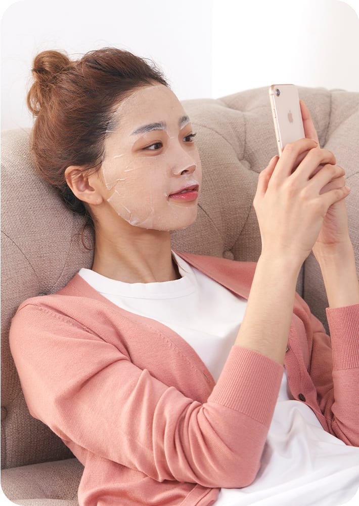 제품을 얼굴에 바르고 쇼파에 앉아 핸드폰을 보면서 쉬고 있는 모델